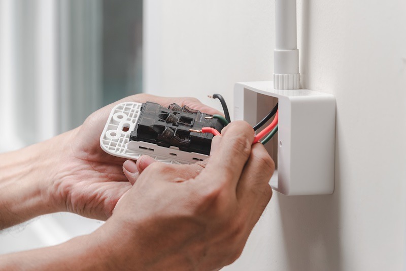 The electrician plugs the power cord into the wall outlet.